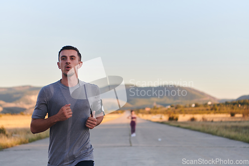 Image of A handsome young couple running together during the early morning hours, with the mesmerizing sunrise casting a warm glow, symbolizing their shared love and vitality