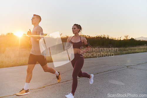 Image of A handsome young couple running together during the early morning hours, with the mesmerizing sunrise casting a warm glow, symbolizing their shared love and vitality