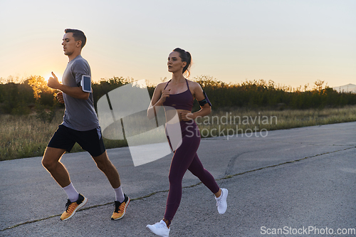 Image of A handsome young couple running together during the early morning hours, with the mesmerizing sunrise casting a warm glow, symbolizing their shared love and vitality