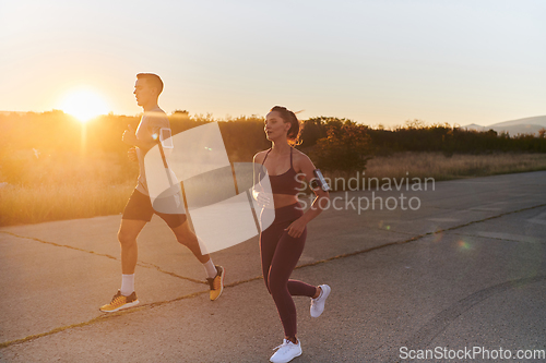 Image of A handsome young couple running together during the early morning hours, with the mesmerizing sunrise casting a warm glow, symbolizing their shared love and vitality