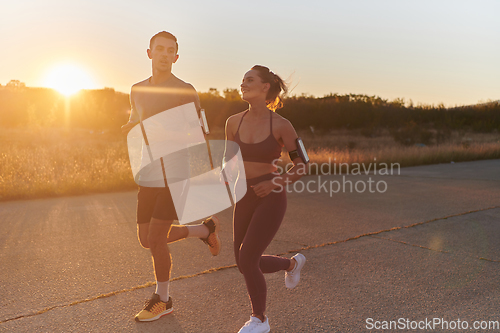 Image of A handsome young couple running together during the early morning hours, with the mesmerizing sunrise casting a warm glow, symbolizing their shared love and vitality