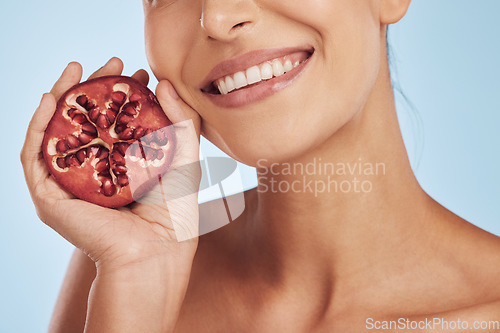 Image of Smile, skincare and hands of woman with pomegranate in studio isolated on a blue background. Natural, fruit and face of model with food for nutrition, healthy vegan diet and vitamin c for wellness.