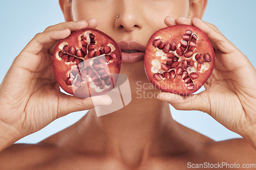 Image of Hands, skincare and woman with pomegranate for beauty in studio isolated on a blue background. Natural, fruit and face of model with food for nutrition, healthy vegan diet and vitamin c for wellness