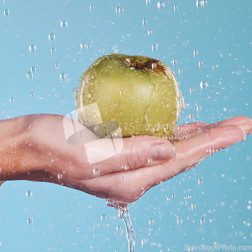 Image of Health, water and a hand with an apple on a blue background for nutrition, cleaning or wellness. Diet, food and closeup of a person with a fruit in palm for a detox isolated on a studio backdrop