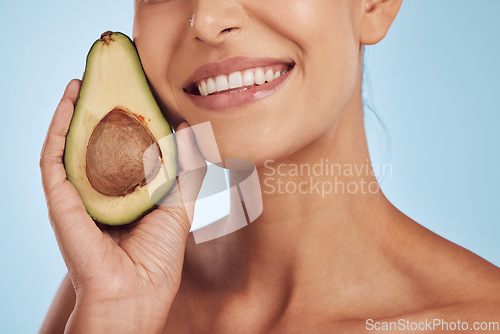 Image of Skincare, beauty and smile, woman with avocado, natural makeup and facial detox on blue background. Health, wellness and mouth of model, organic luxury cleaning and cosmetics with fruit in studio.