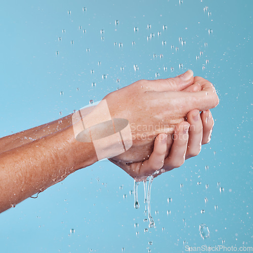 Image of Water drops, hygiene and a person washing hands in studio on a blue background for cleaning or hydration. Beauty, wellness and skincare with a splash in the bathroom for sustainability or health