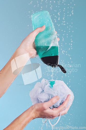 Image of Woman, hands and loofah with soap in shower for hygiene, washing or cleaning body against a blue studio background. Closeup of female person pouring gel bottle with falling water or rain on sponge