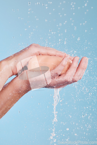 Image of Water, soap and a person washing hands in studio on a blue background for hygiene or hydration. Cleaning, wellness and skincare with an adult in the bathroom to remove bacteria or germs for health