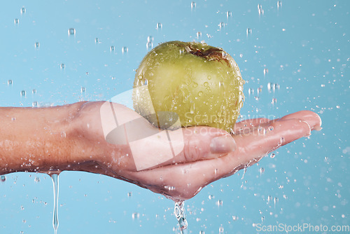 Image of Vegan, water and a hand with an apple on a blue background for nutrition, cleaning or wellness. Diet, food and closeup of a person with a fruit in palm for a detox isolated on a studio backdrop