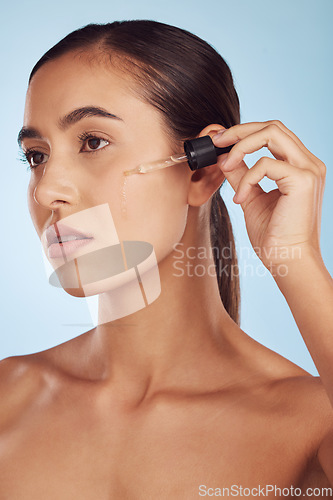 Image of Face, skincare and serious woman with serum for beauty in studio isolated on a blue background. Cosmetics, model and essential oil, collagen and hyaluronic acid for dermatology, health and wellness.