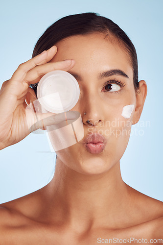 Image of Portrait, beauty and woman with cream, dermatology and skincare on a blue studio background. Face, female person and model with lotion, cosmetics and wellness with creme, pouting and luxury product