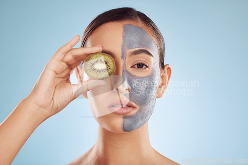 Image of Portrait, kiwi and mask for beauty with a woman in studio on a blue background for antiaging skincare. Face, facial and fruit with an attractive young female holding a berry for natural treatment