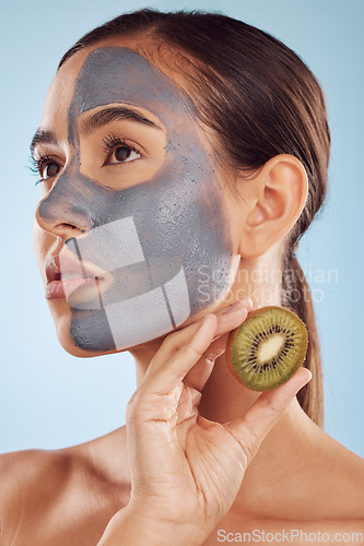 Image of Thinking, kiwi and mask for beauty with a woman in studio on a blue background for antiaging skincare. Face, facial and fruit with a young female model holding a berry for natural organic treatment