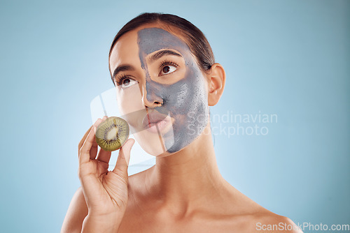 Image of Thinking, kiwi and mask for skincare with a woman in studio on a blue background for antiaging treatment. Face, facial and pout with an attractive young female holding a berry for natural beauty