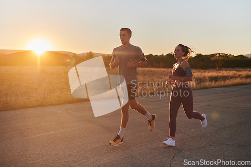 Image of A handsome young couple running together during the early morning hours, with the mesmerizing sunrise casting a warm glow, symbolizing their shared love and vitality