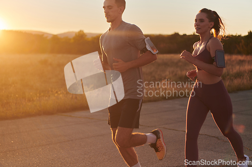 Image of A handsome young couple running together during the early morning hours, with the mesmerizing sunrise casting a warm glow, symbolizing their shared love and vitality