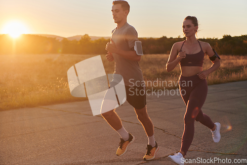 Image of A handsome young couple running together during the early morning hours, with the mesmerizing sunrise casting a warm glow, symbolizing their shared love and vitality