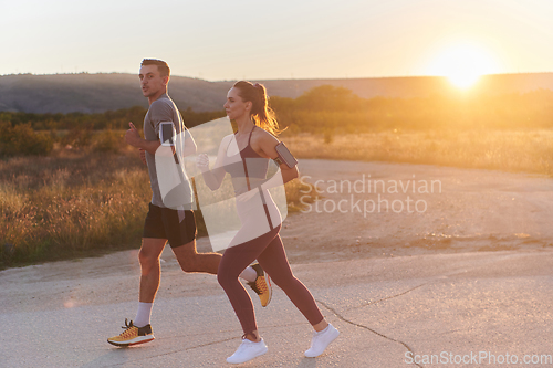 Image of A handsome young couple running together during the early morning hours, with the mesmerizing sunrise casting a warm glow, symbolizing their shared love and vitality