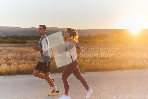 Image of A handsome young couple running together during the early morning hours, with the mesmerizing sunrise casting a warm glow, symbolizing their shared love and vitality