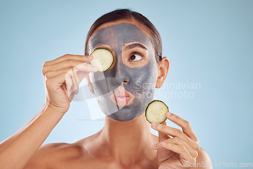 Image of Face, cucumber and mask for beauty with a woman in studio on a blue background for antiaging skincare. Facial, idea and pout with an attractive young female holding a vegetable for natural treatment