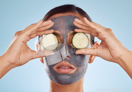 Image of Face mask, skincare and woman with cucumber on eyes for beauty in studio isolated on a blue background. Cosmetics, model and clay facial treatment with fruit, food and dermatology, health or wellness