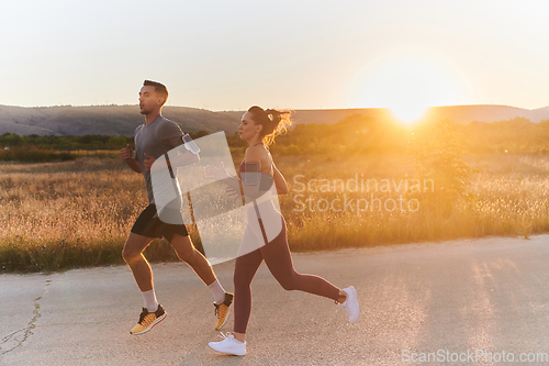 Image of A handsome young couple running together during the early morning hours, with the mesmerizing sunrise casting a warm glow, symbolizing their shared love and vitality