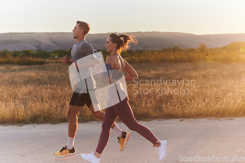 Image of A handsome young couple running together during the early morning hours, with the mesmerizing sunrise casting a warm glow, symbolizing their shared love and vitality