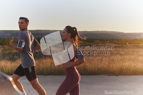 Image of A handsome young couple running together during the early morning hours, with the mesmerizing sunrise casting a warm glow, symbolizing their shared love and vitality