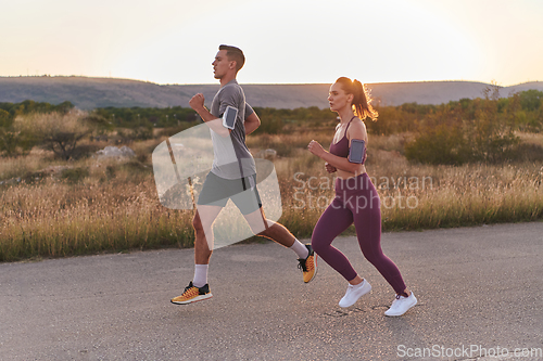 Image of A handsome young couple running together during the early morning hours, with the mesmerizing sunrise casting a warm glow, symbolizing their shared love and vitality