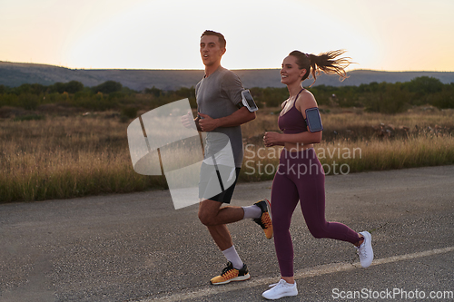 Image of A handsome young couple running together during the early morning hours, with the mesmerizing sunrise casting a warm glow, symbolizing their shared love and vitality