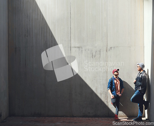 Image of Fashion, friends and men in a city talking, bond and hanging out on the weekend against wall background. Chilling, conversation and male people downtown for fun, freedom and off day with trendy style