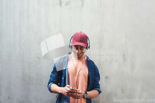 Image of Happy, music and a man with a phone on a wall for social media, communication or a chat. Smile, technology and a male college student streaming or listening to a podcast on a mobile app with space