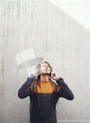 Image of Man is listening to music, student with headphones on university campus and future mindset against wall background. Gen z, education and male person at college, mockup space and podcast streaming