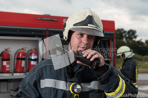 Image of fireman using walkie talkie at rescue action fire truck and fireman's team in background.