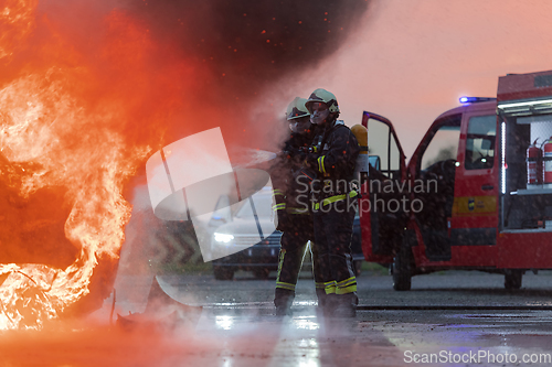 Image of Firefighters using water fire extinguisher to fighting with the fire flame in car accident. Firefighter industrial and public safety concept rescue in night.