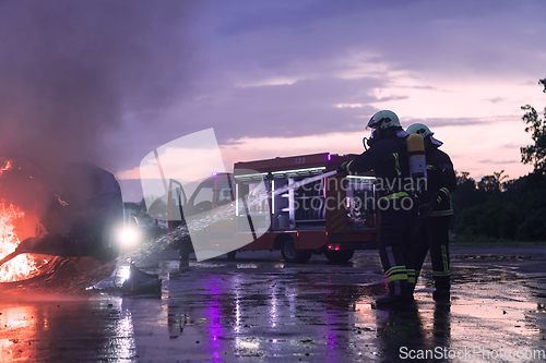 Image of Firefighters using water fire extinguisher to fighting with the fire flame in car accident. Firefighter industrial and public safety concept rescue in night.