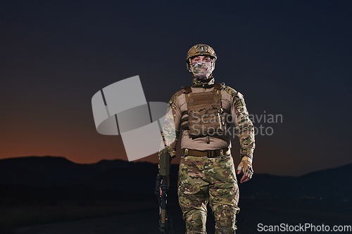 Image of A professional soldier in full military gear striding through the dark night as he embarks on a perilous military mission