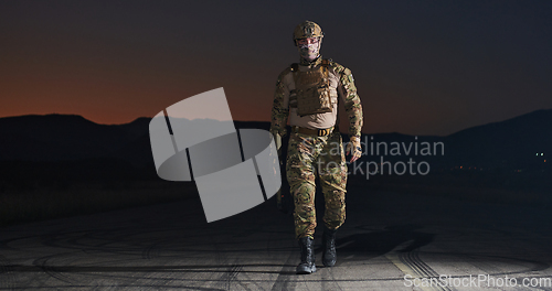 Image of A professional soldier in full military gear striding through the dark night as he embarks on a perilous military mission