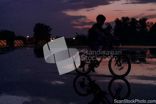 Image of Lonely children silhouette on bike, boy riding bicycle on reflective water. Background beautiful sunset.