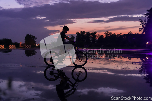 Image of Lonely children silhouette on bike, boy riding bicycle on reflective water. Background beautiful sunset.