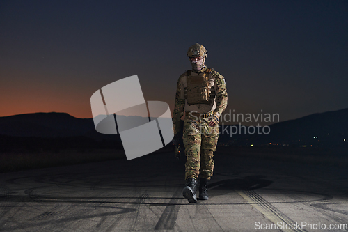 Image of A professional soldier in full military gear striding through the dark night as he embarks on a perilous military mission