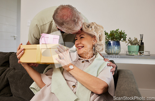 Image of Gift, surprise and a senior couple on their anniversary for celebration in their home living room together. Love, present and birthday with a husband giving his wife a box while sitting on a sofa