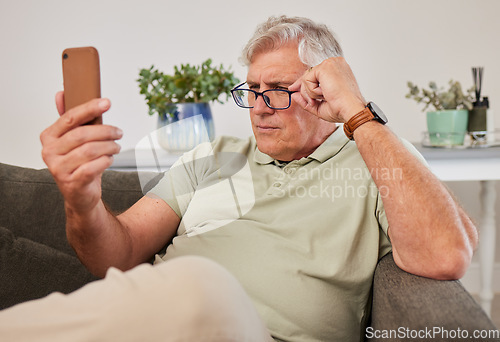 Image of Phone, glasses and senior man reading a text message, blog or online news on a sofa in the living room. Vision, technology and elderly male person squinting while networking on a cellphone at home.
