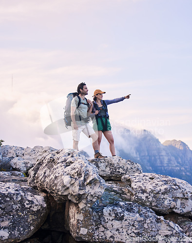 Image of Mountains, hiking and pointing, man and woman on peak for adventure in nature, landscape and travel. Outdoor trekking, couple on cliff and relax in scenic clouds for natural journey, view and looking