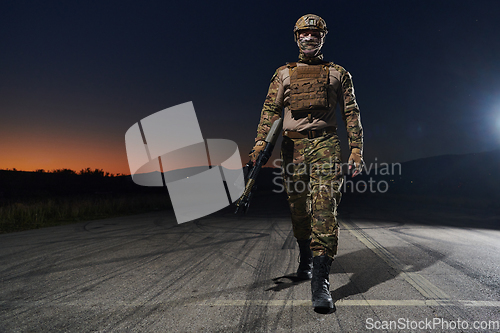 Image of A professional soldier in full military gear striding through the dark night as he embarks on a perilous military mission