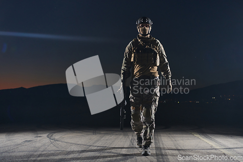 Image of A professional soldier in full military gear striding through the dark night as he embarks on a perilous military mission