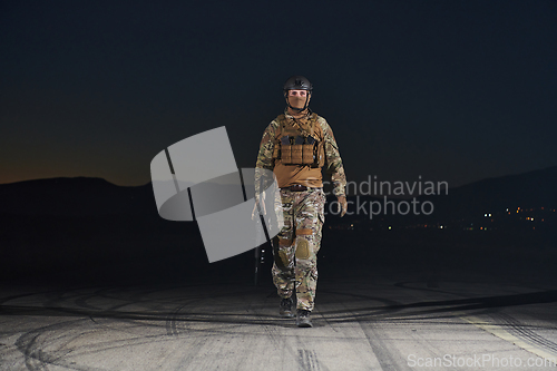 Image of A professional soldier in full military gear striding through the dark night as he embarks on a perilous military mission