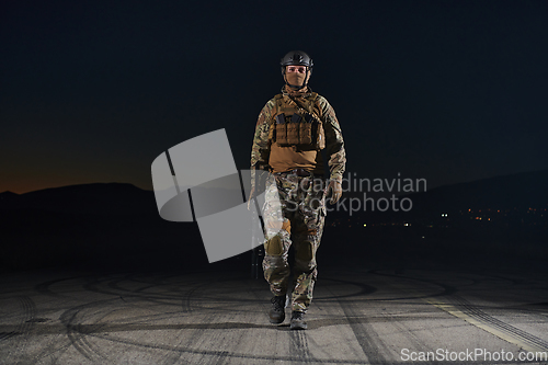 Image of A professional soldier in full military gear striding through the dark night as he embarks on a perilous military mission
