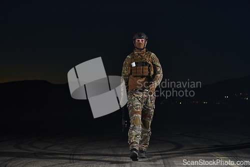 Image of A professional soldier in full military gear striding through the dark night as he embarks on a perilous military mission