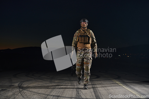 Image of A professional soldier in full military gear striding through the dark night as he embarks on a perilous military mission